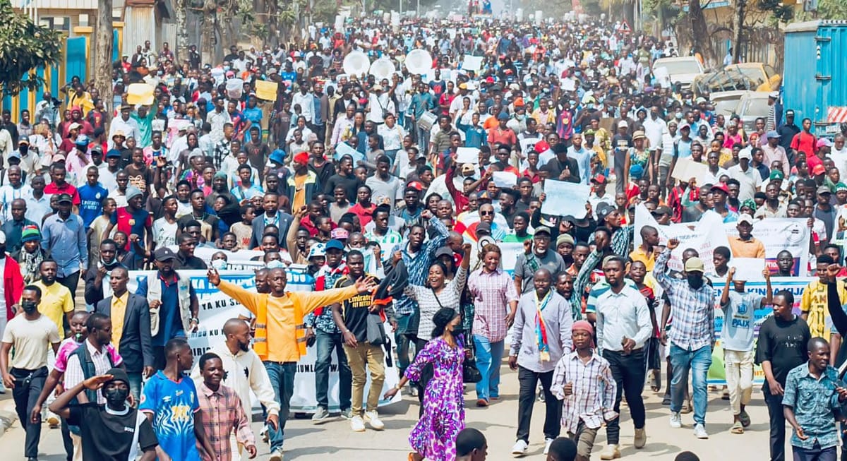Une foule compacte de manifestants remplit une avenue de Goma, poings levés et banderoles déployées
