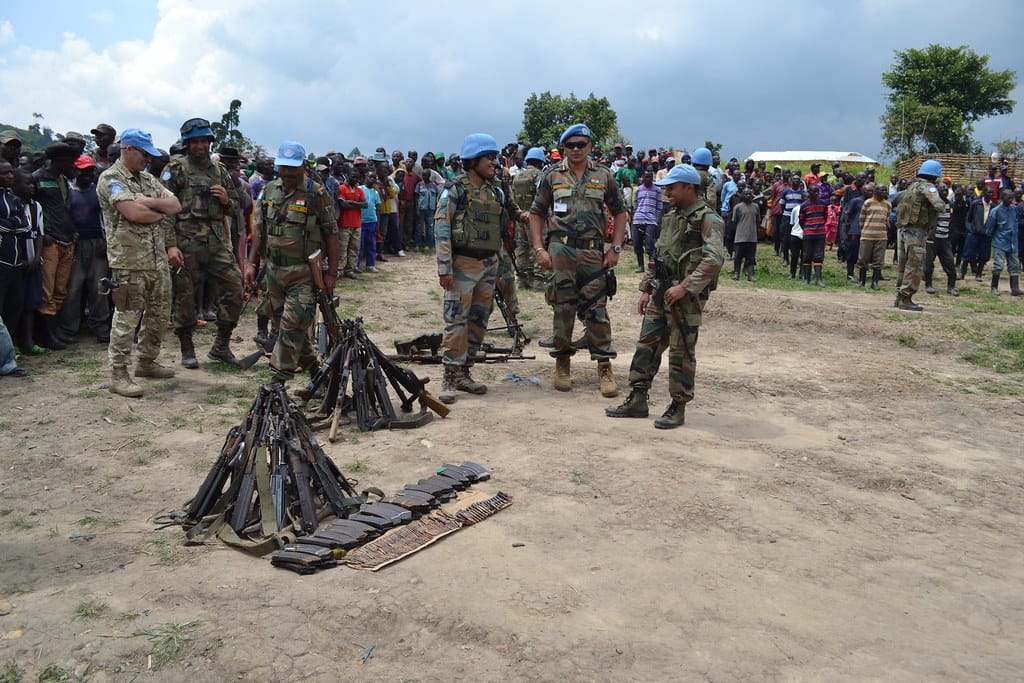 Des Casques bleus de la MONUSCO entourent des armes déposées au sol lors d’une cérémonie de remise d’armes au Nord-Kivu, devant une foule d’habitants